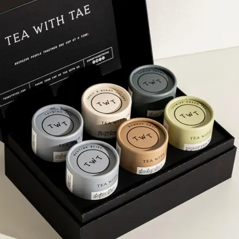 Assorted premium tea sampler tins arranged in a sleek black gift box with branded lid