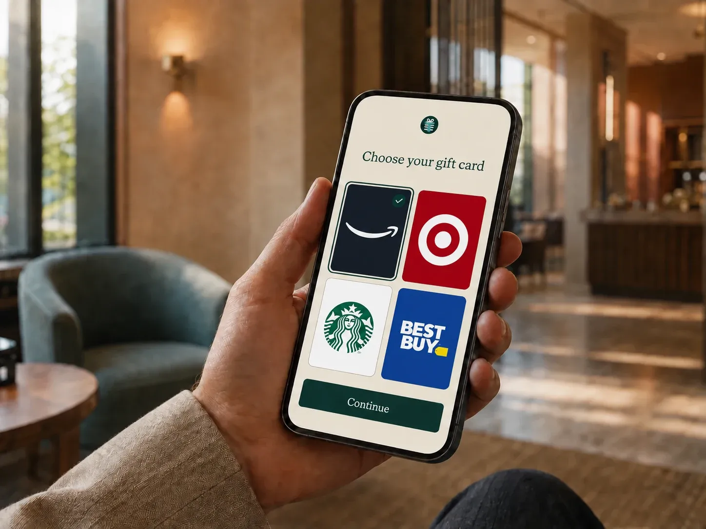 A person holding a phone showing digital gift cards from Amazon.com, Target, Starbucks, and Best Buy, with Amazon.com selected.